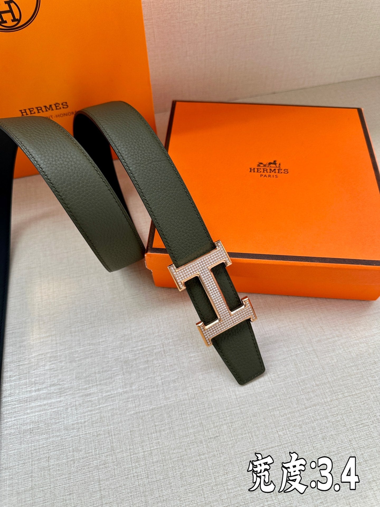 Hermes leather belt buckle detail with dark green strap and rose-gold H emblem.