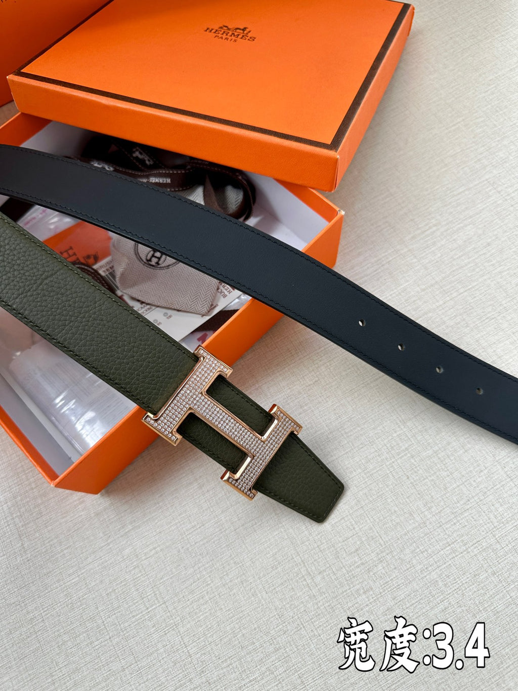 Hermes leather belt with dark green strap and rose-gold H buckle, flat-lay view.