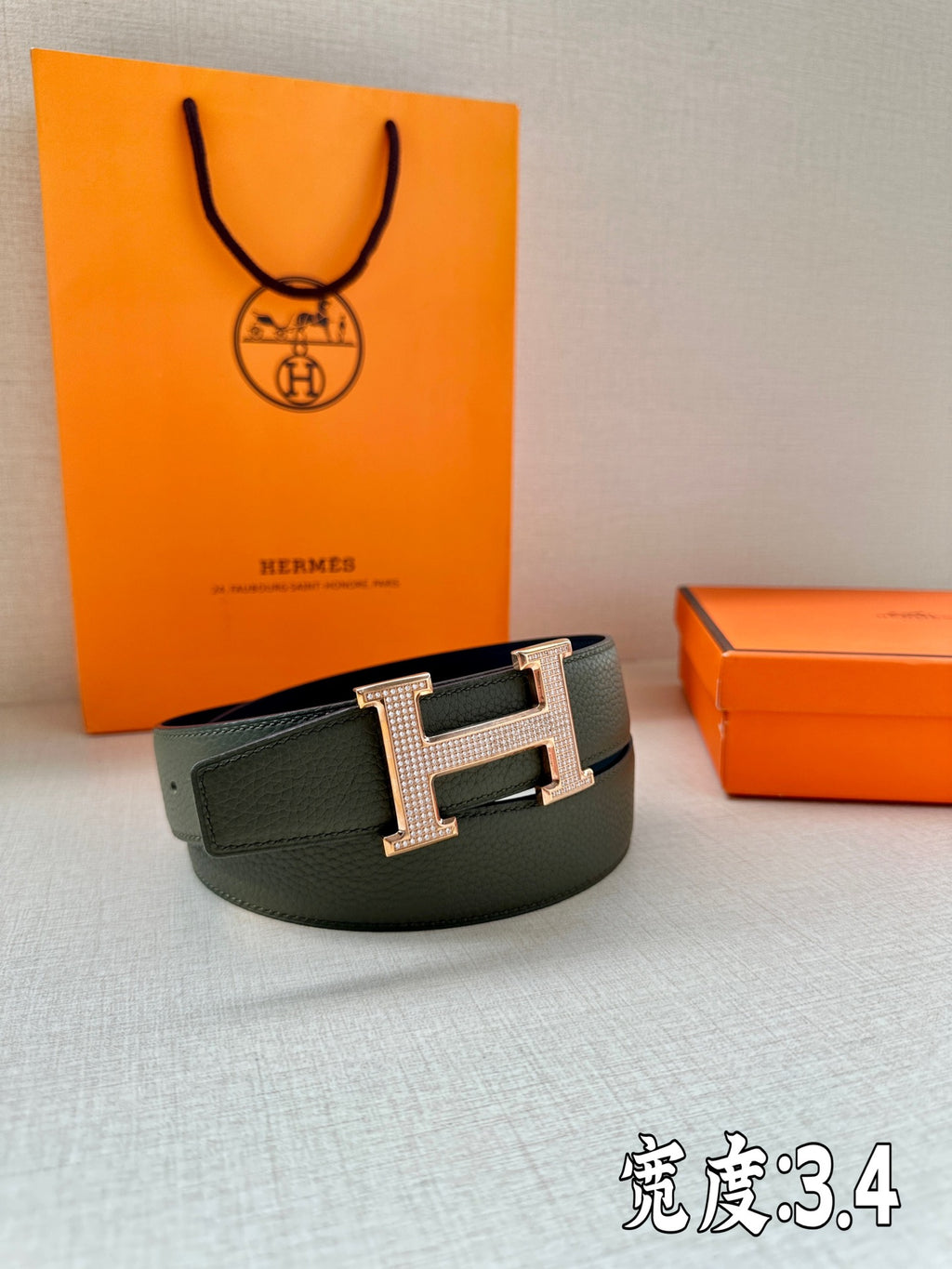 Hermes leather belt in dark green with studded H buckle, centered on display surface.