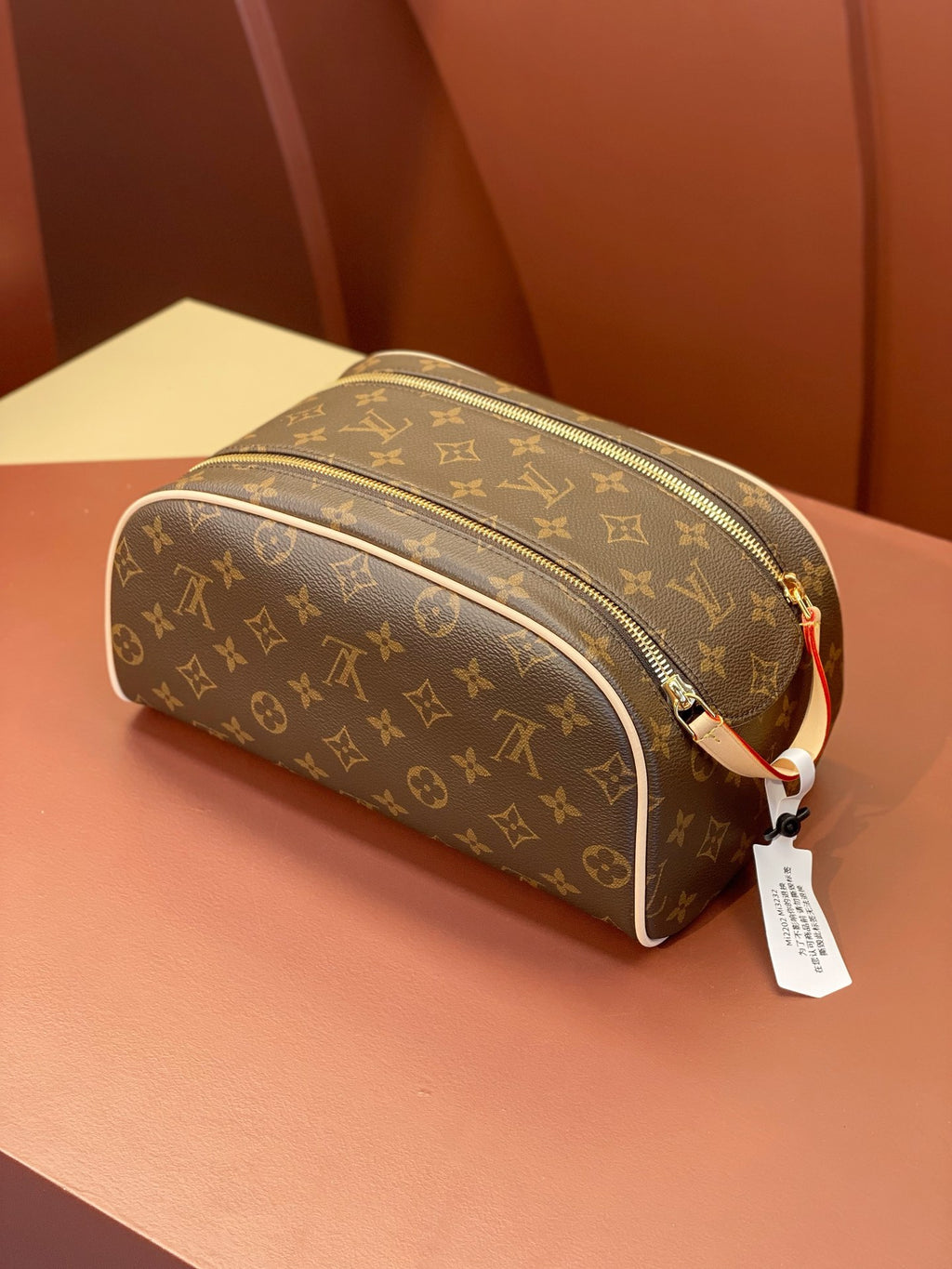 Louis Vuitton monogram toiletry bag with top zip, red-and-white strap, hanging tag