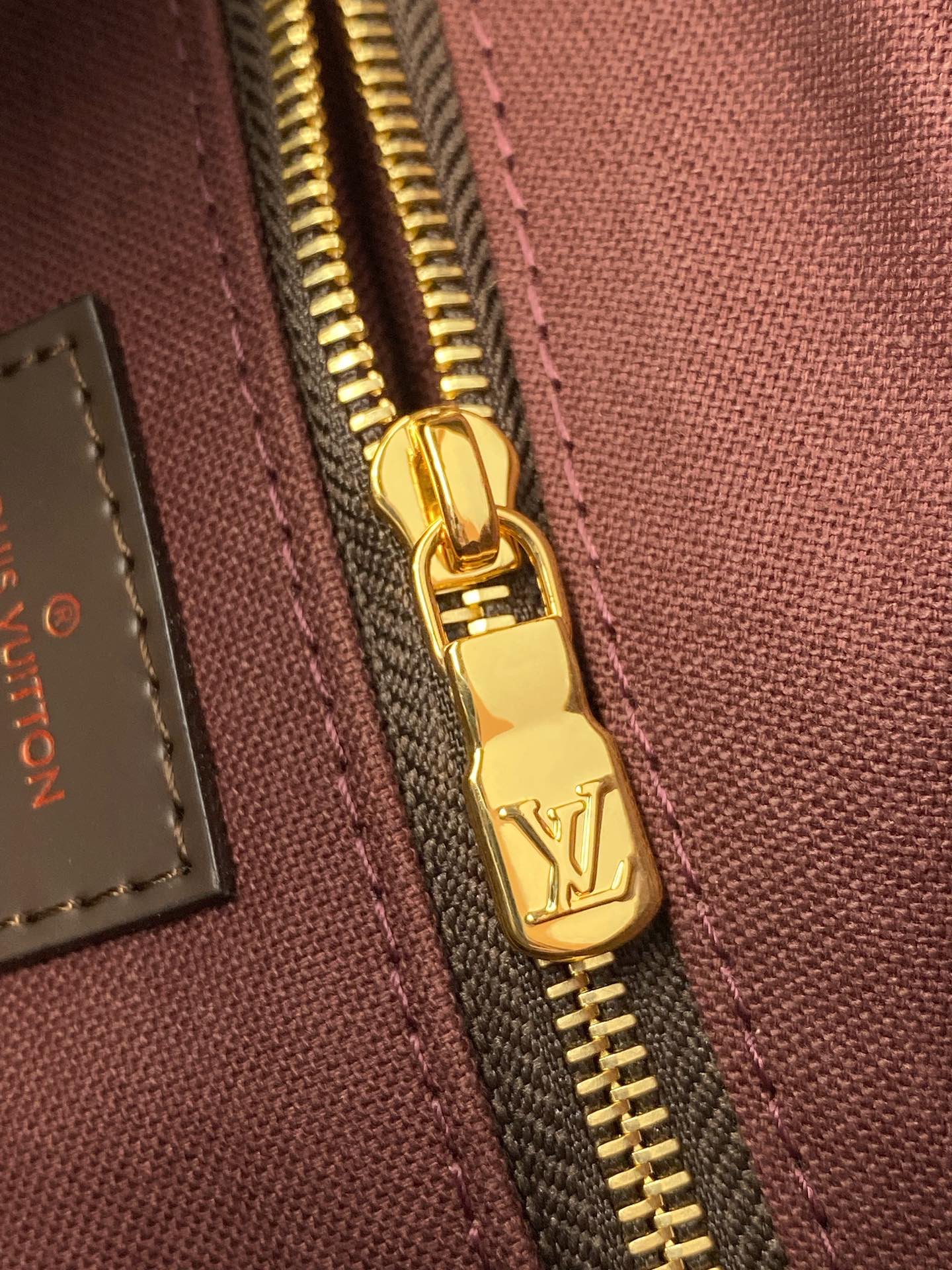 Louis Vuitton gold zipper pull with LV logo on maroon-lined toiletry bag.