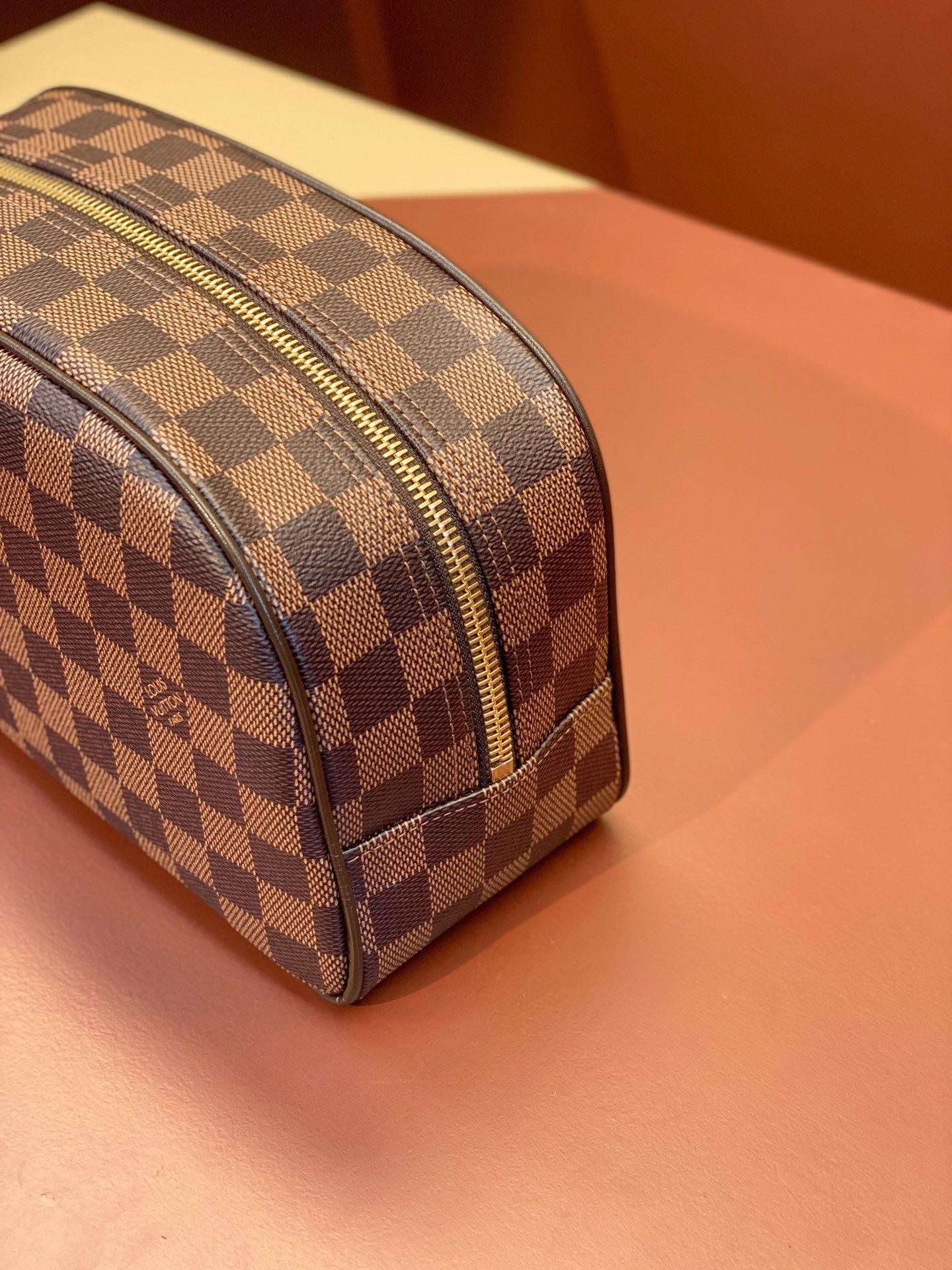 Louis Vuitton Damier checkered toiletry bag side view with gold-tone zipper track.