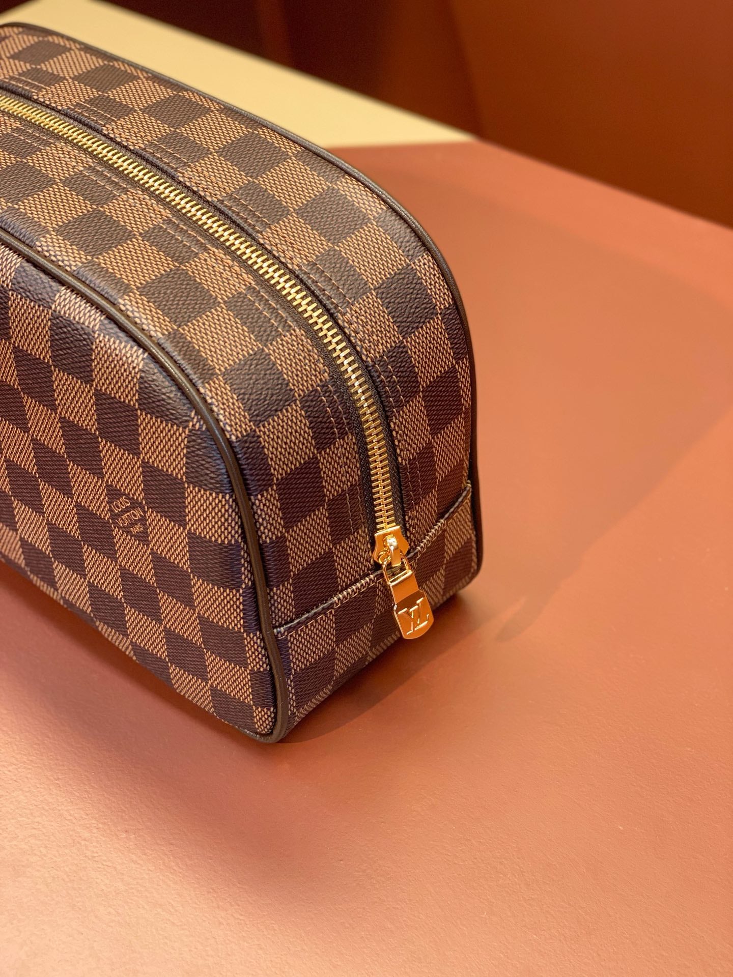Louis Vuitton Damier checkered toiletry bag corner view with gold zipper pull.