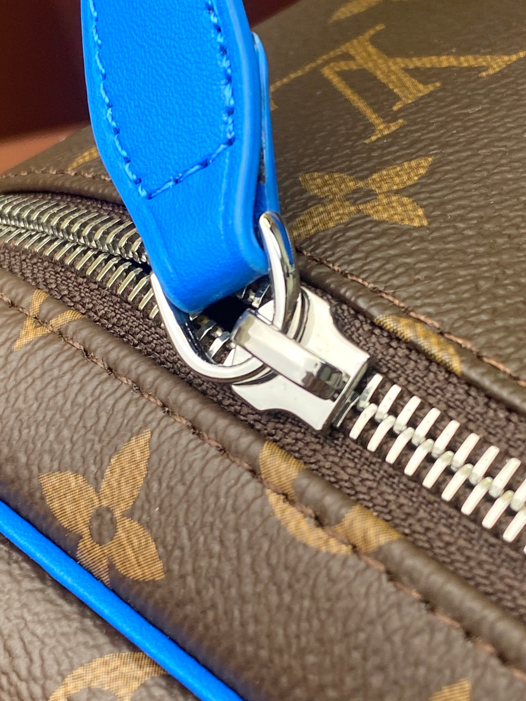 Close-up of blue leather trim and metal zipper hardware on Louis Vuitton bag
