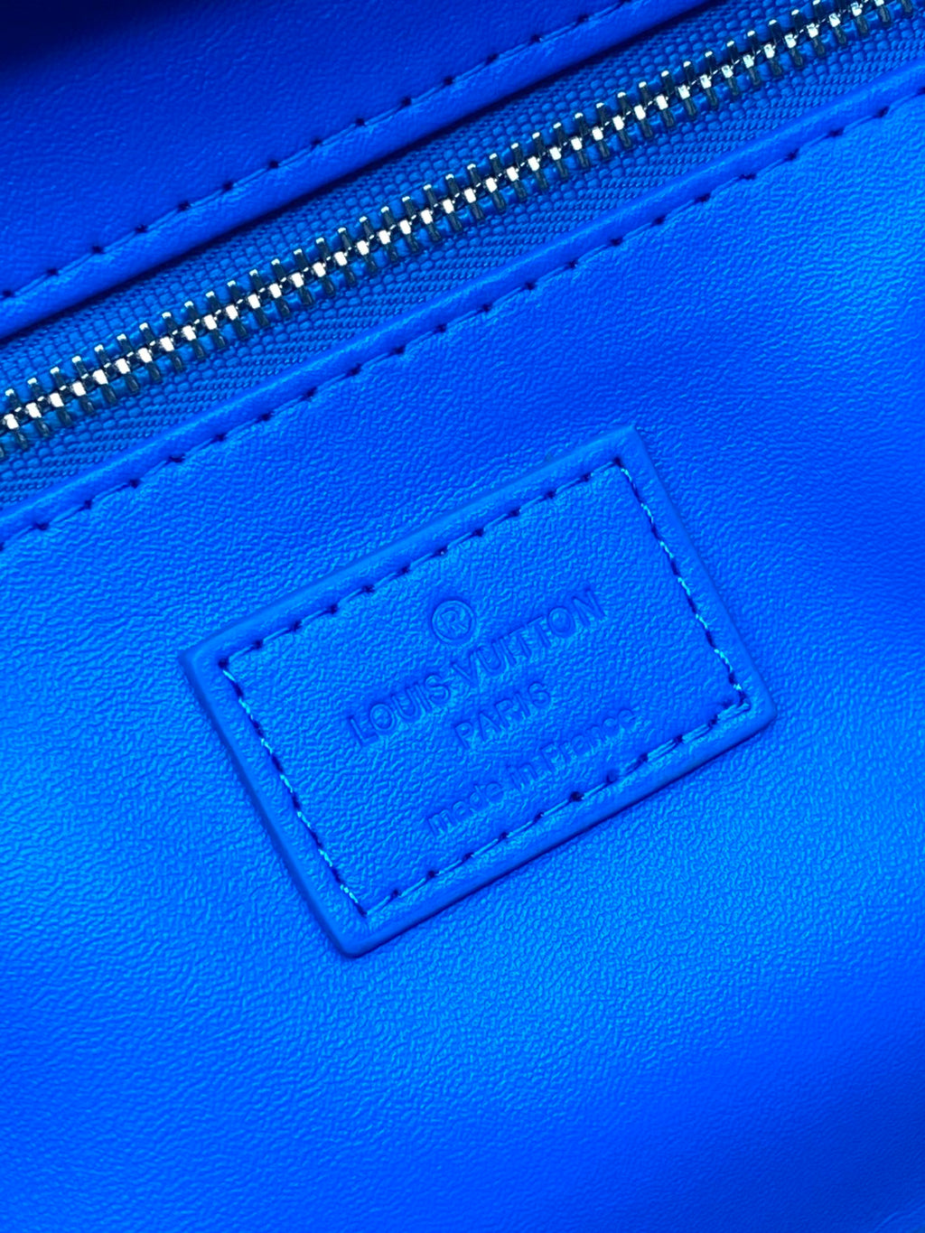 Blue leather label on Louis Vuitton monogram bag near the top zipper seam