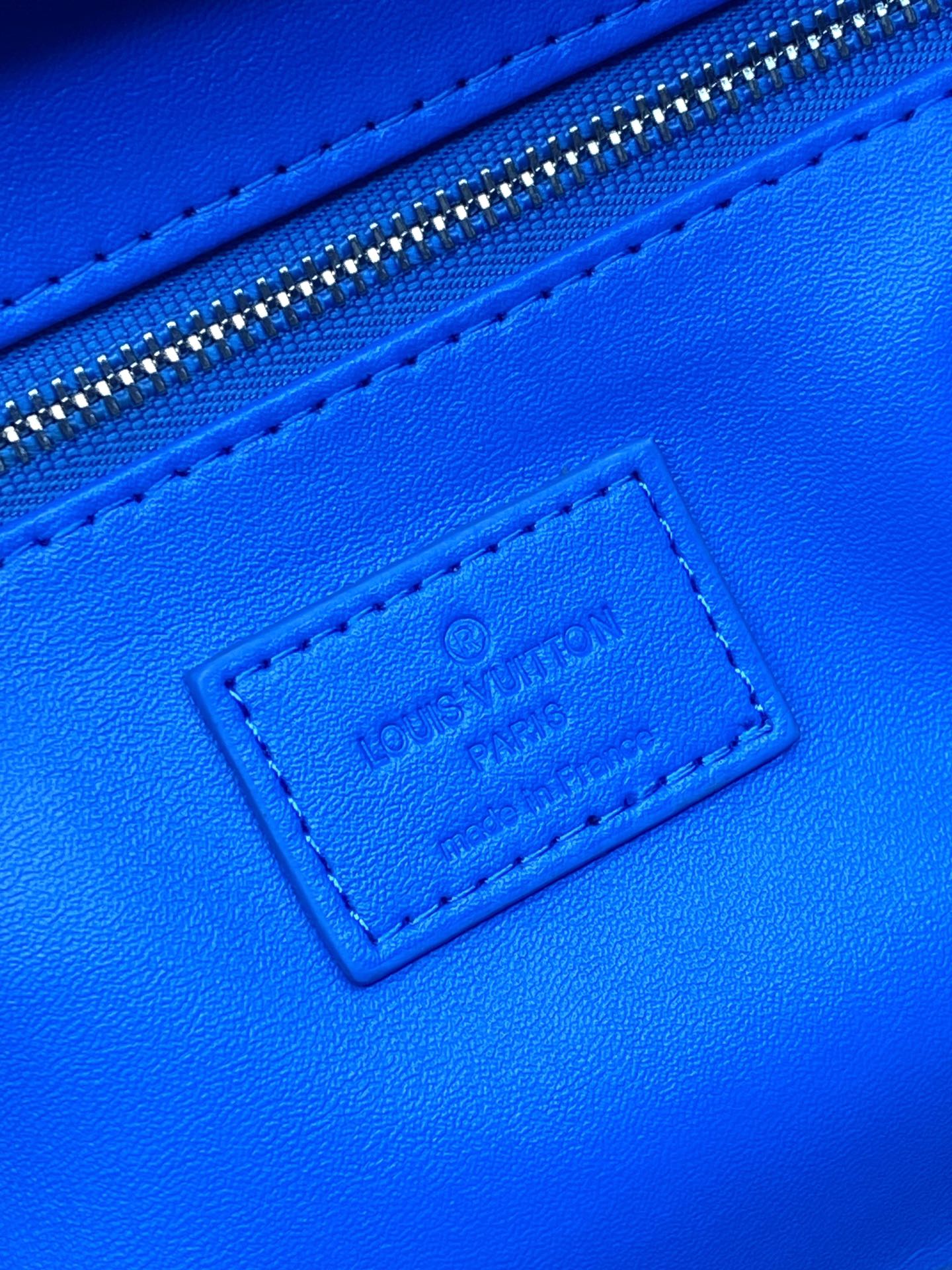 Blue leather label on Louis Vuitton monogram bag near the top zipper seam
