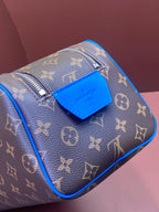 Louis Vuitton monogram bag with blue front patch and top zipper, angled view