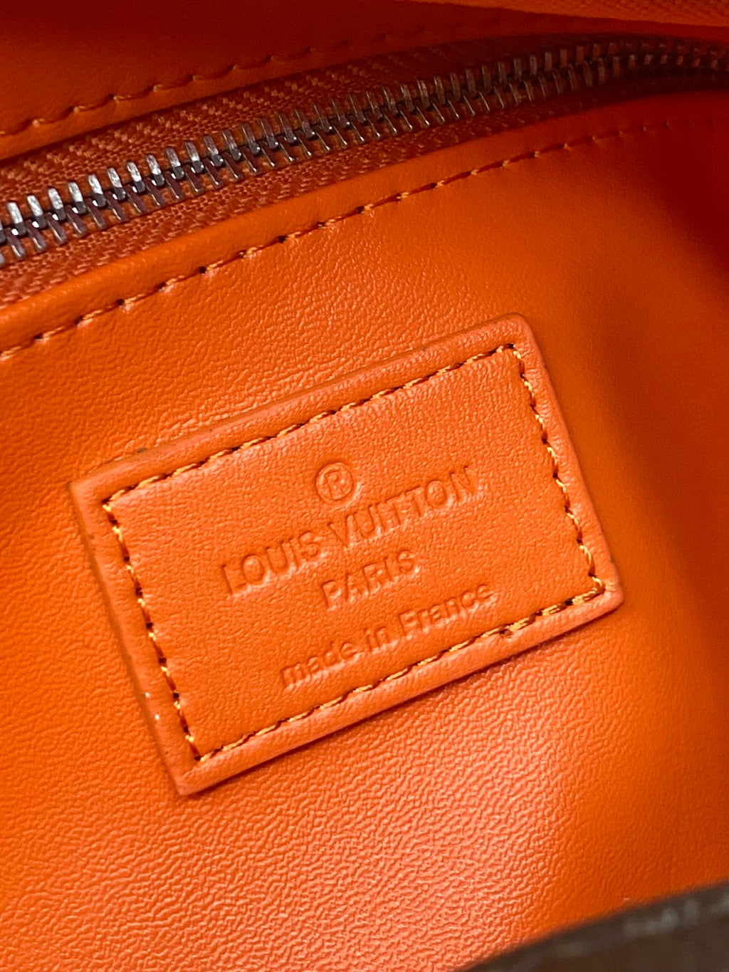 Louis Vuitton logo leather label on orange-trim bag, gold-tone text