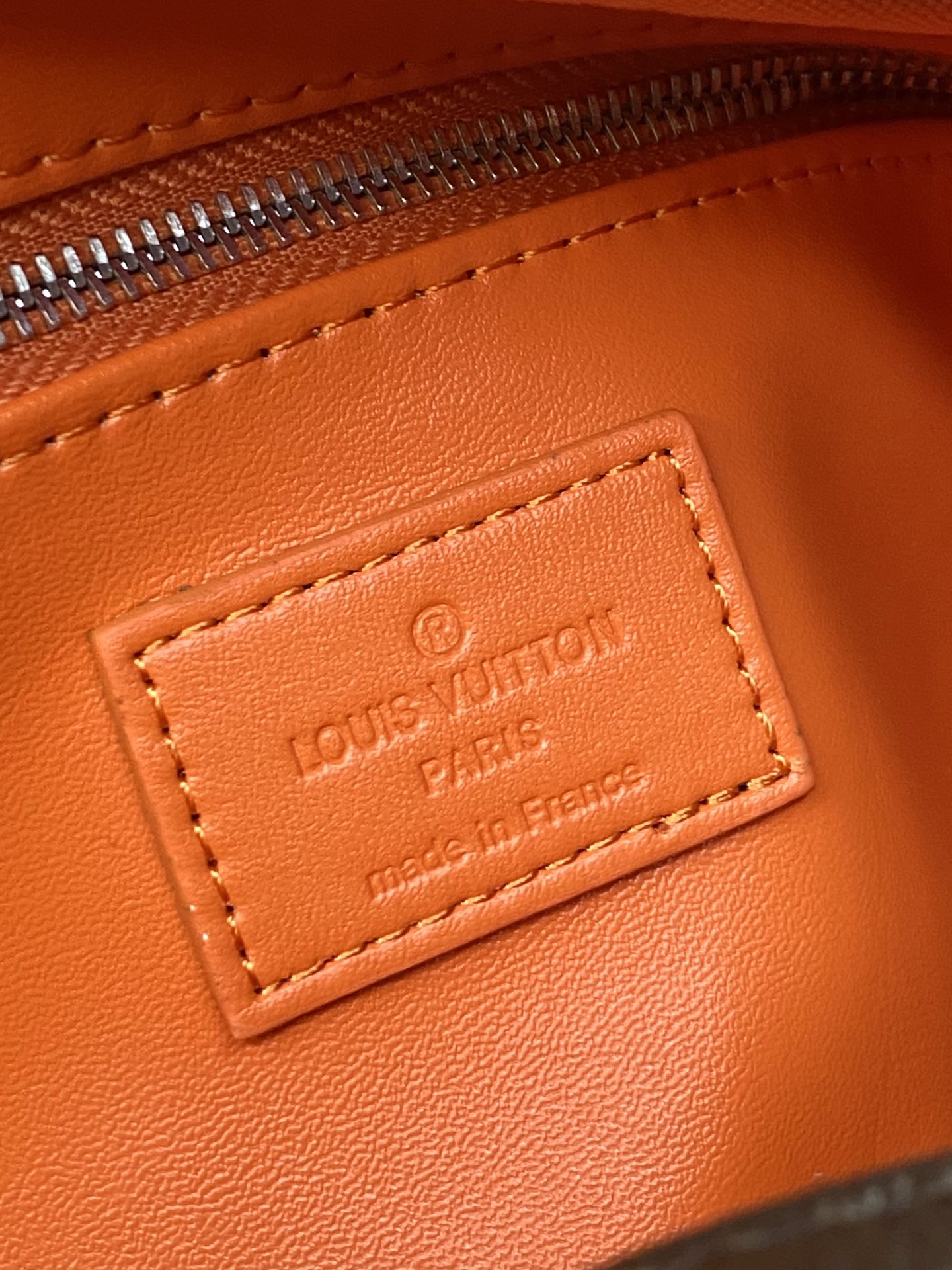 Louis Vuitton logo leather label on orange-trim bag, gold-tone text