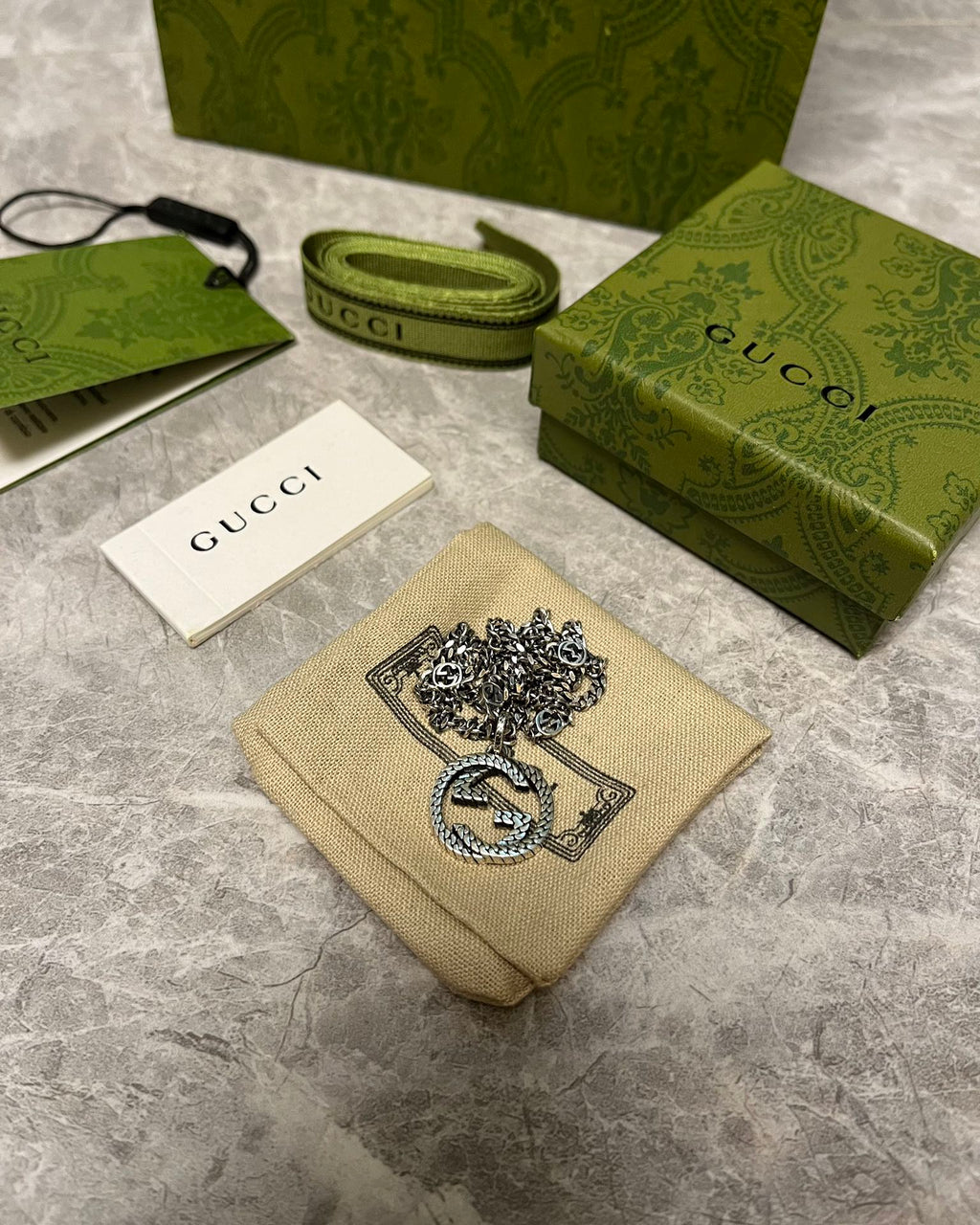 Silver-toned chain necklace with GG heart pendant on beige pouch