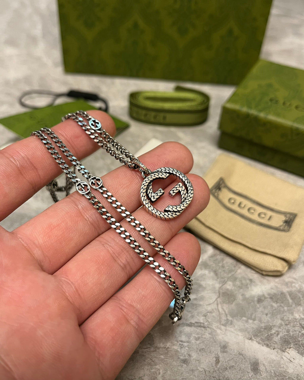 Silver-toned chain necklace with oval GG heart pendant, clasp visible