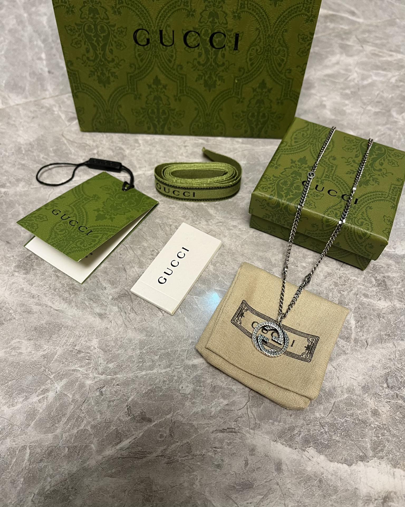 Silver-toned chain necklace with GG heart pendant on beige Gucci pouch
