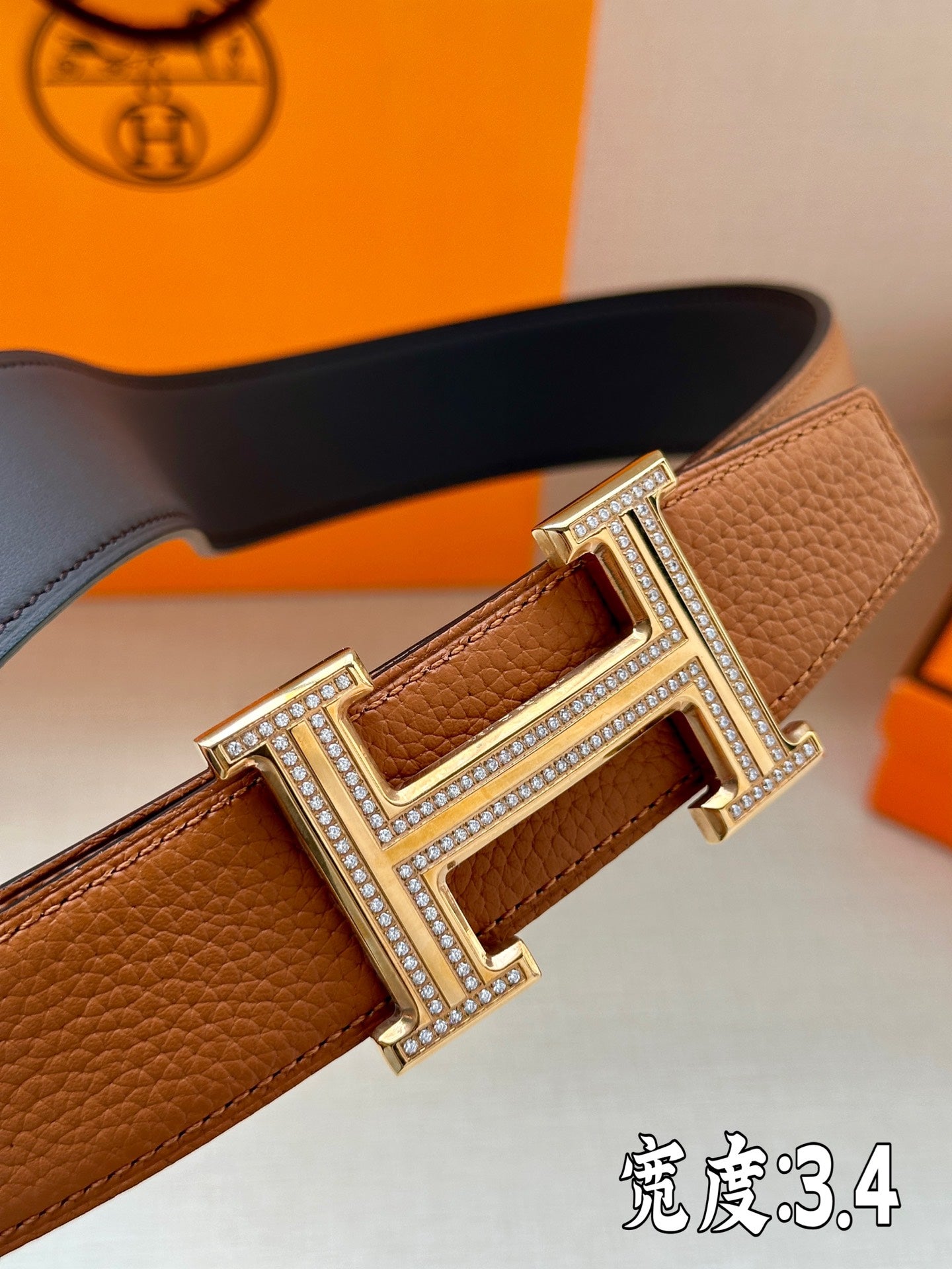 Brown leather belt close-up: silver-toned H buckle with rhinestone trim