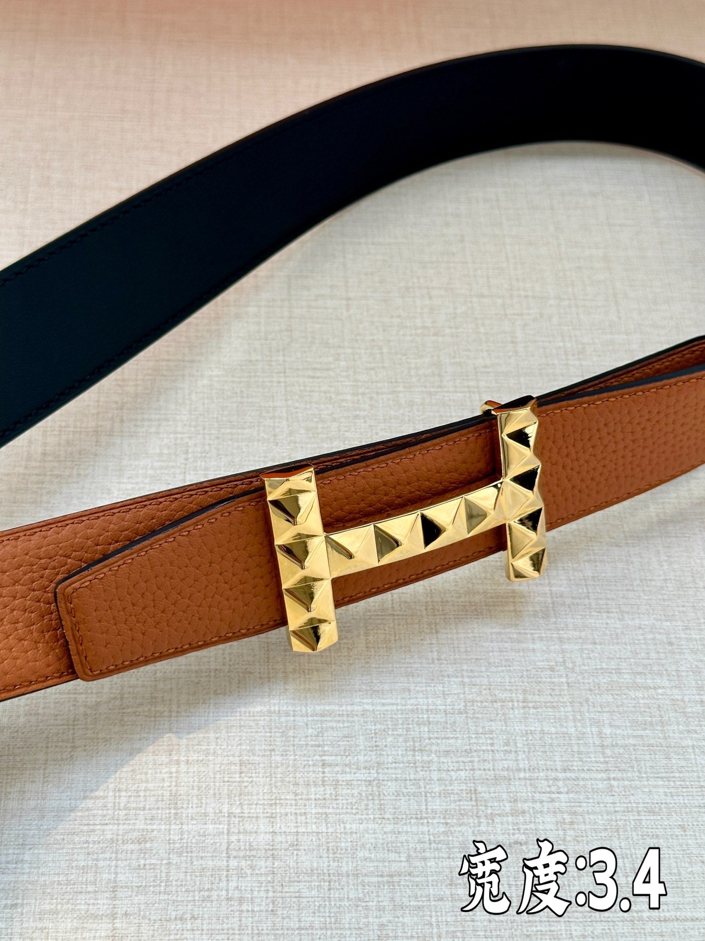 Hermes leather belt buckle detail with tan strap and gold-tone pyramid studs