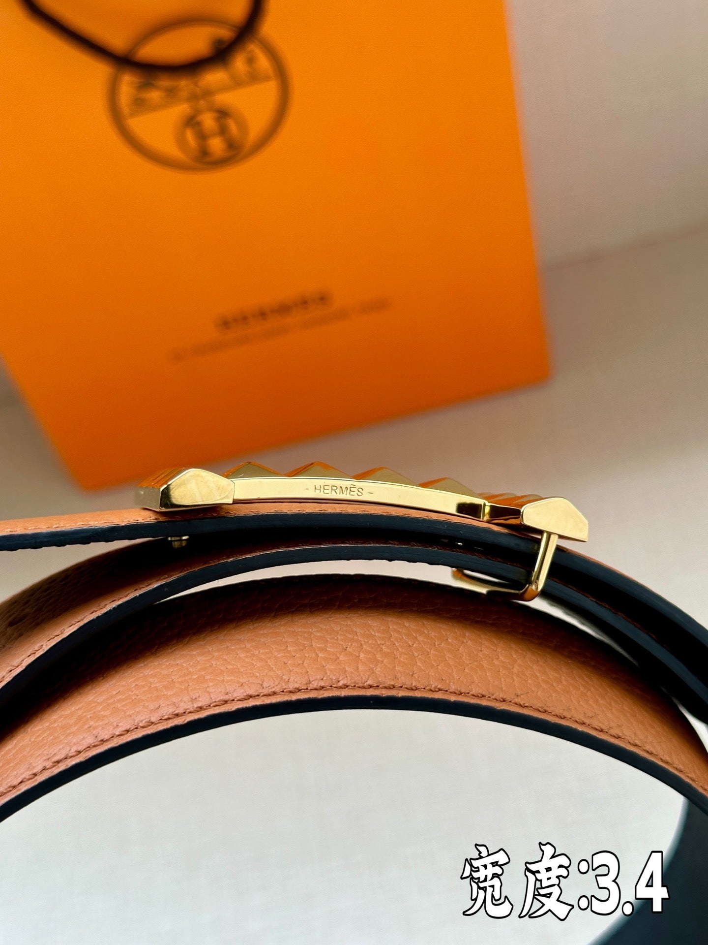 Hermes leather belt close-up with black strap and gold-tone studded buckle