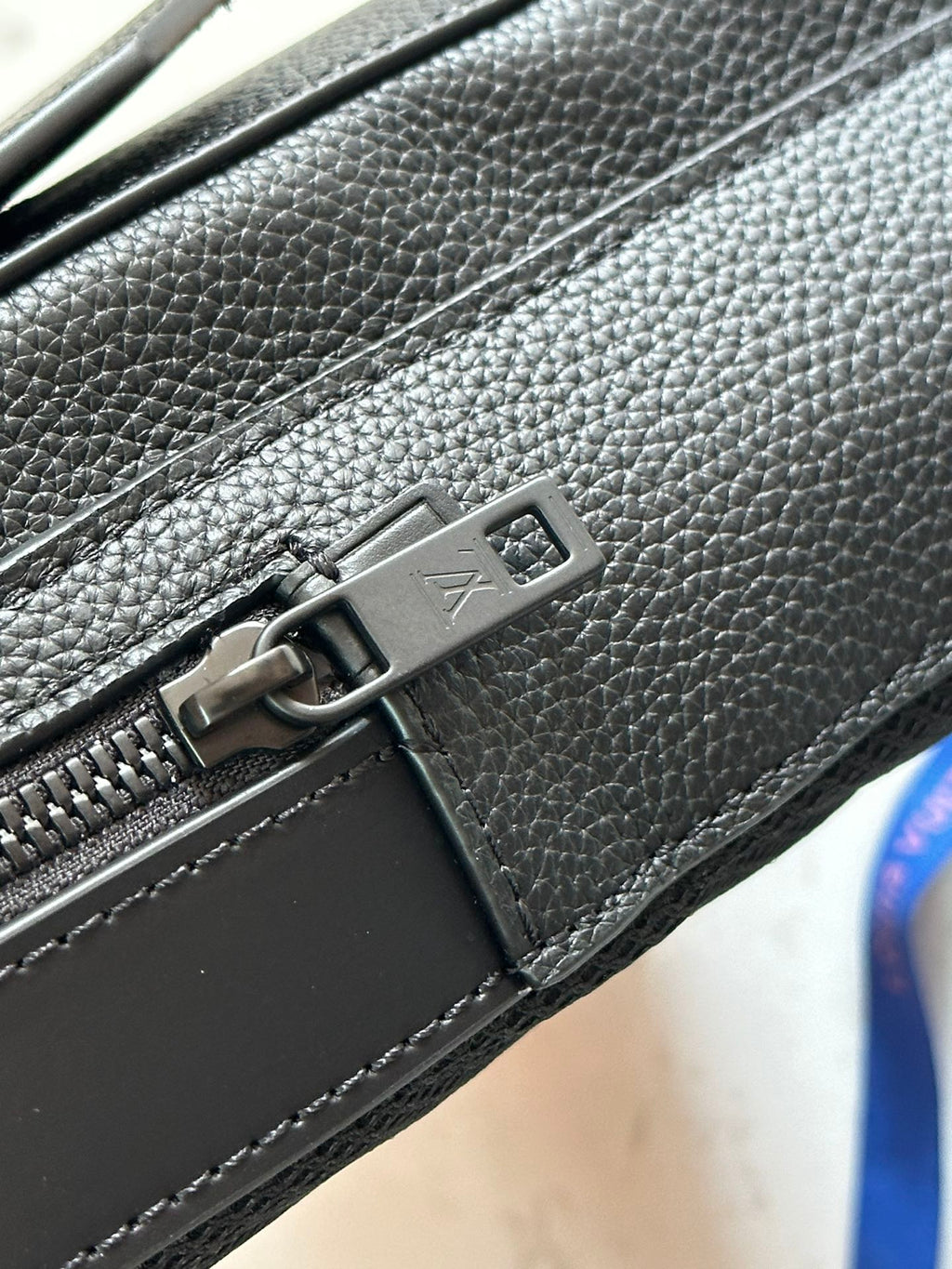 Louis Vuitton leather bag corner with metal buckle and zipper pull on textured dark gray