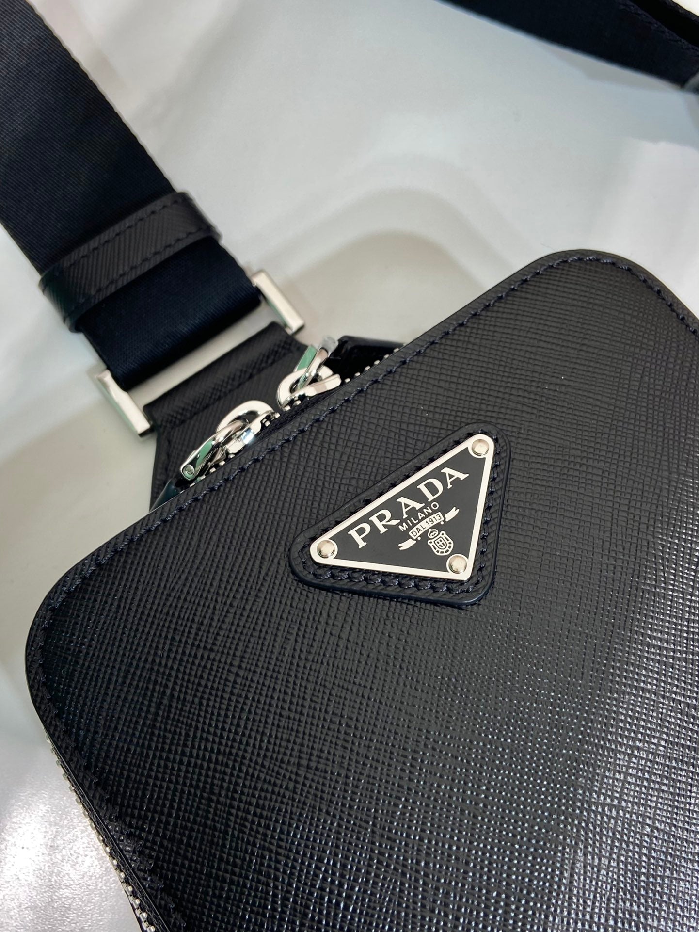Prada black leather crossbody bag close-up with PRADA triangular logo plaque