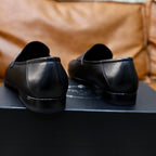 Black leather loafers, rear view with low heel on a product box