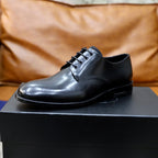 Prada unisex lace-up oxfords in dark shiny leather on black shoe box, front view.