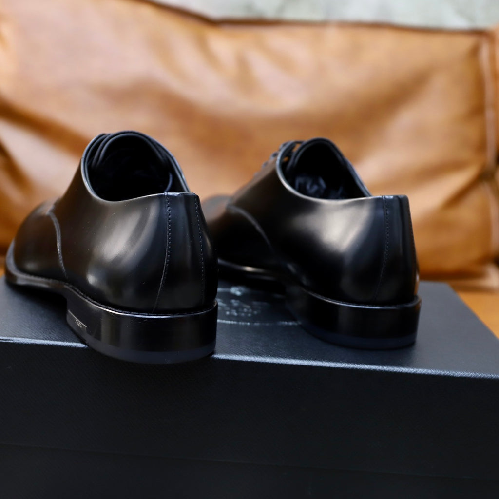 Prada unisex leather oxfords in dark finish, heel view on black shoe box.