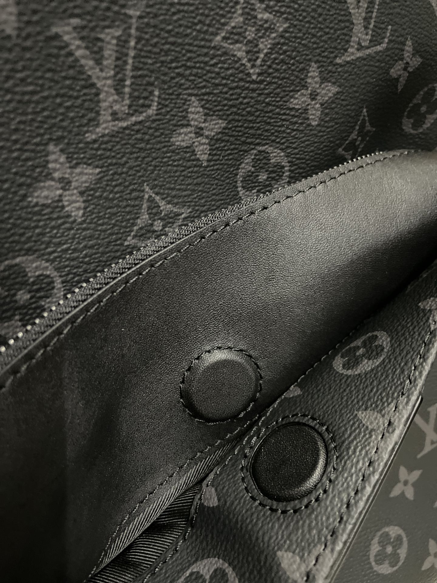 Black monogram zipper pull and stitched snap detail on a leather-look bag