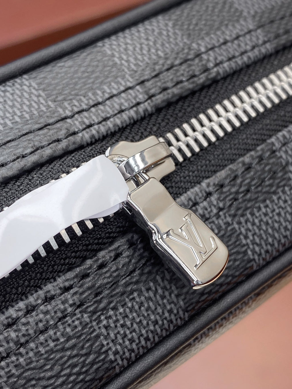 Louis Vuitton metal zipper pull on dark gray check bag, close-up.