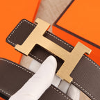 Hermes belt buckle close-up with dark brown leather, white stitching, and silver hardware