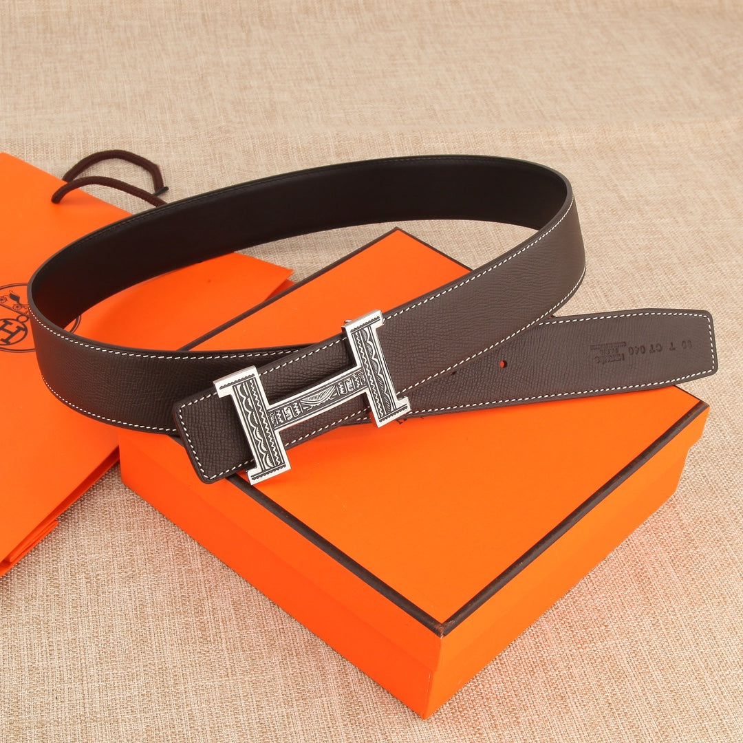 Brown leather belt laid flat with ornate silver buckle and keeper panel