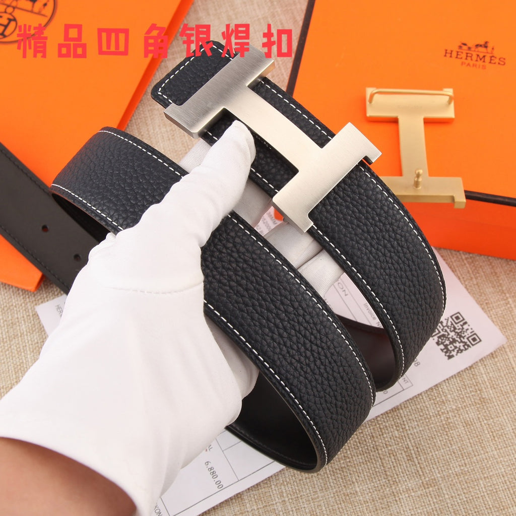 Black pebbled leather belt with gold-tone H buckle, gloved hand holding strap