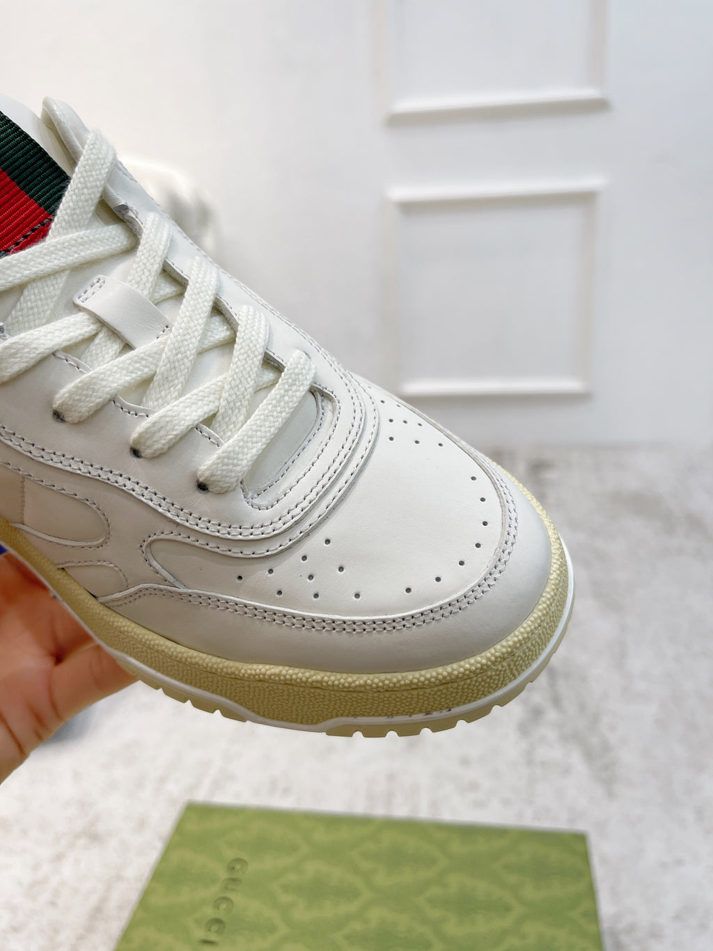 Unisex white sneaker close-up with laces, perforated toe, and beige sole