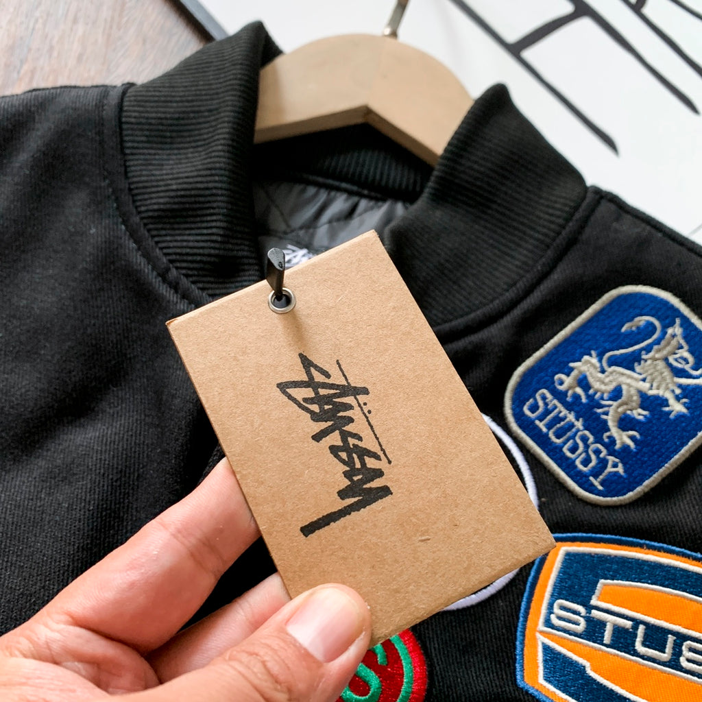 Black bomber jacket close-up with tag and embroidered crest patches