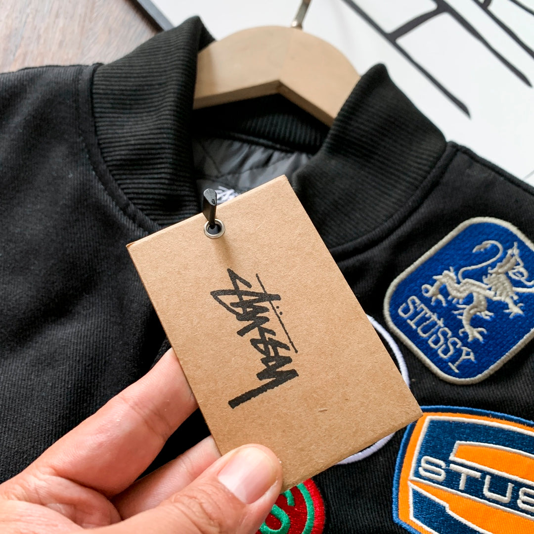 Black bomber jacket close-up with tag and embroidered crest patches