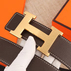 Leather belt detail: gold-tone H buckle and dark strap with white stitched edges