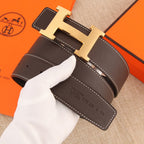 Leather belt with gold H buckle, dark strap with subtle embossed marks, white stitching