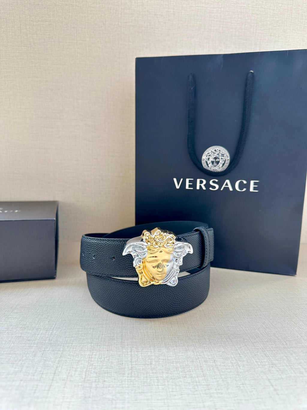 Versace navy belt with Medusa buckle in front of a gift bag