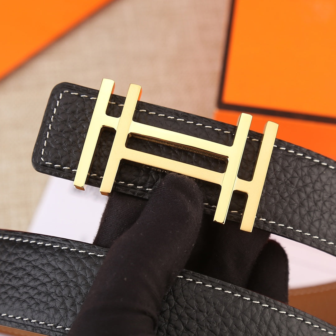 Black belt buckle close-up with gold-tone metal H and white edge stitching