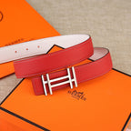 Red leather belt with gold H buckle and white stitching; engraved logo patch visible.