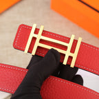 Red belt buckle detail with gold metal H bar and white edge stitching.