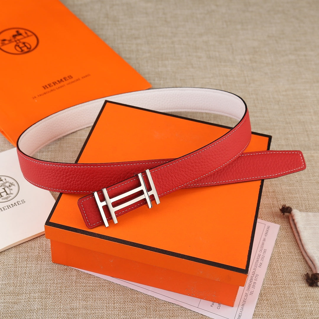 Red leather belt with gold H buckle, laid across a white inner strap.