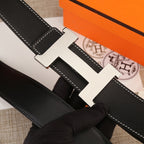 Gold H buckle detail on black leather belt with white stitched edges