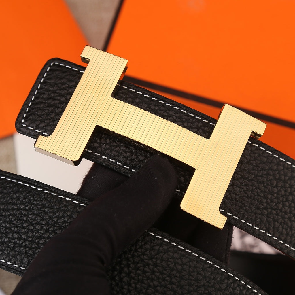 Hermes belt buckle close-up: black textured leather with white stitching and gold H