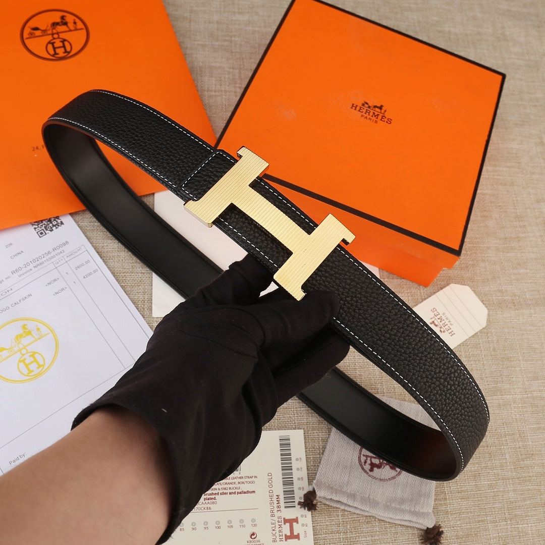 Hermes belt held in hand: black textured leather with white stitching and gold H buckle