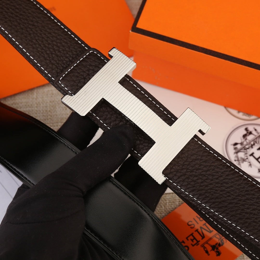 Close-up of leather belt buckle, dark brown strap with white contrast stitching.