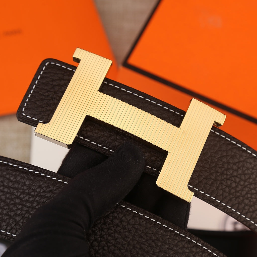 Close-up of H buckle on dark brown leather belt, textured grain and contrast stitching.