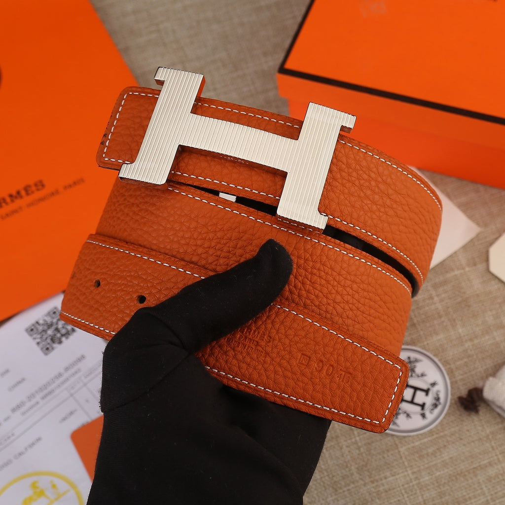 Hermes leather belt with orange textured strap, silver-toned H buckle, stitched edges.