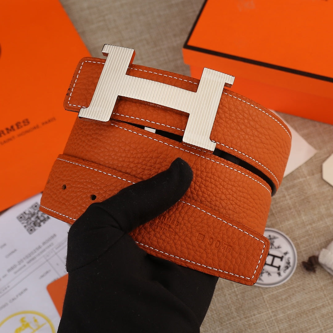 Hermes leather belt with orange textured strap, silver-toned H buckle, stitched edges.