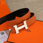 Hermes leather belt in orange with black underside and silver-toned H buckle.