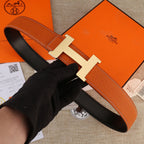 Hermes leather belt with orange strap and silver-toned H buckle on black lining.