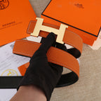 Hermes leather belt with orange strap and silver-toned H buckle, side view.
