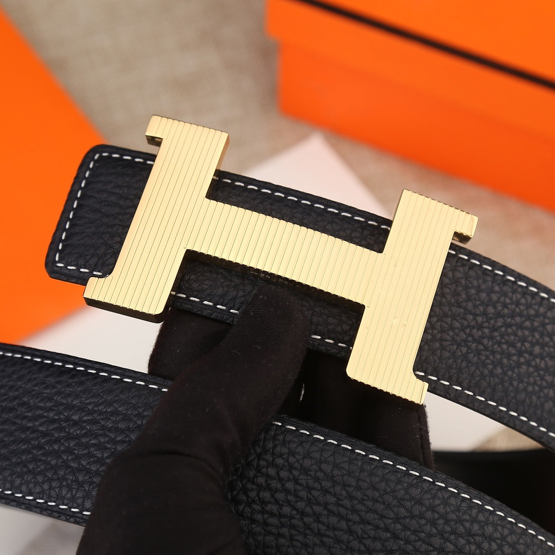 Hermes belt buckle close-up: light gold H with prong detail over black leather stitching.